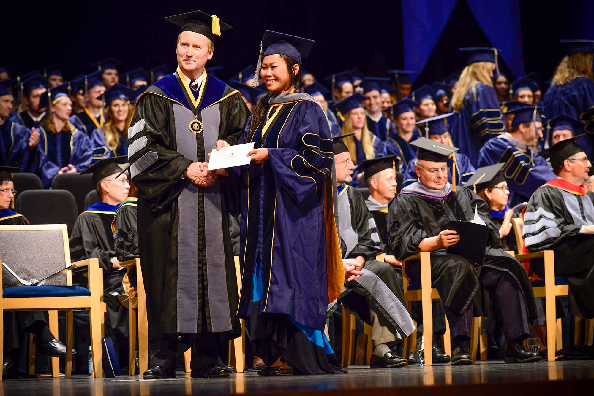 Michael Lairmore shakes hands with a student participating in a graduation ceremony