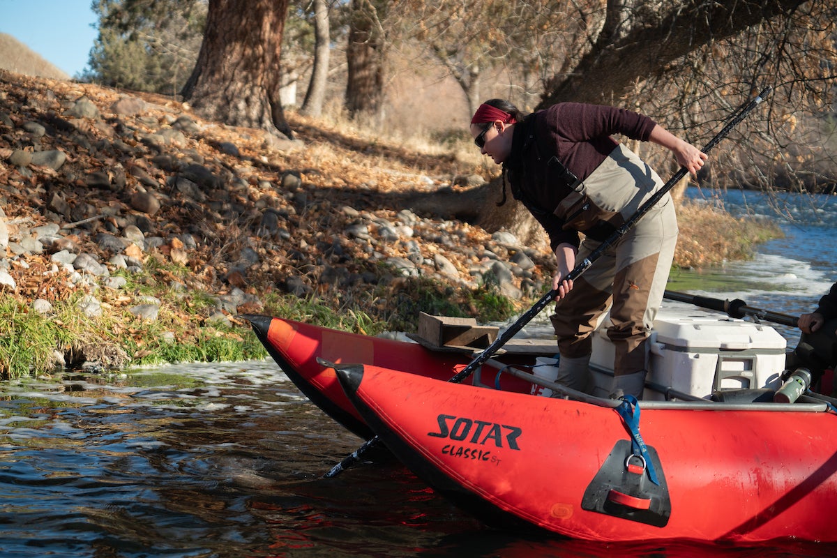 Leanne Knutson of Yurok Tribe leans over red pontoon boat to scoop up dead salmon from Klamath River