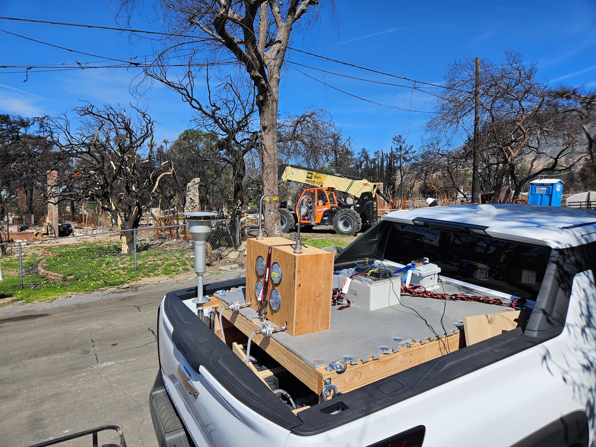 white truck full of air sampling equipment drives along burned trees on a site affected by 2025 Los Angeles fires 