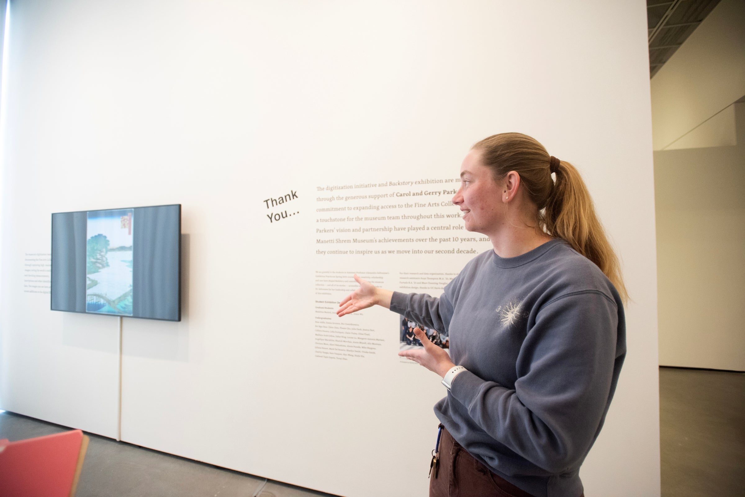 Claire Finley, a sophomore Art History major, gestures to work on gallery wall. 