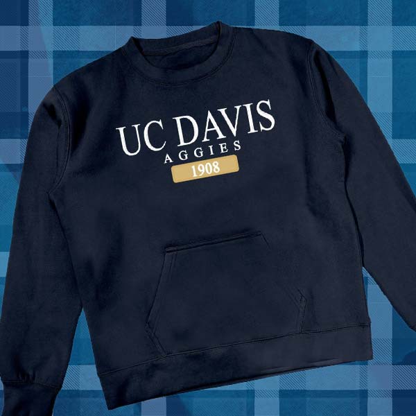 Against an Aggie Blue backdrop is a studio photo of a dark blue sweater that reads UC DAVIS and the year 1908, symbolizing the year the campus was founded.