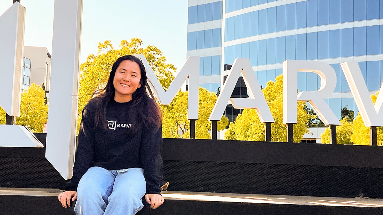 Alexa Kwan sits in front of a company sign for Marvel Technology
