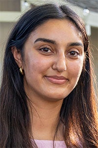 Smiling young woman with long dark hair, gold hoop earrings, soft outdoor lighting