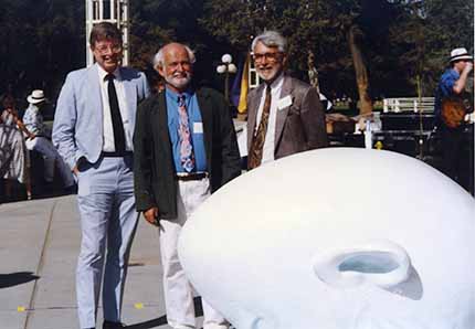 Three people in suits stand next to Egghead sculpture.