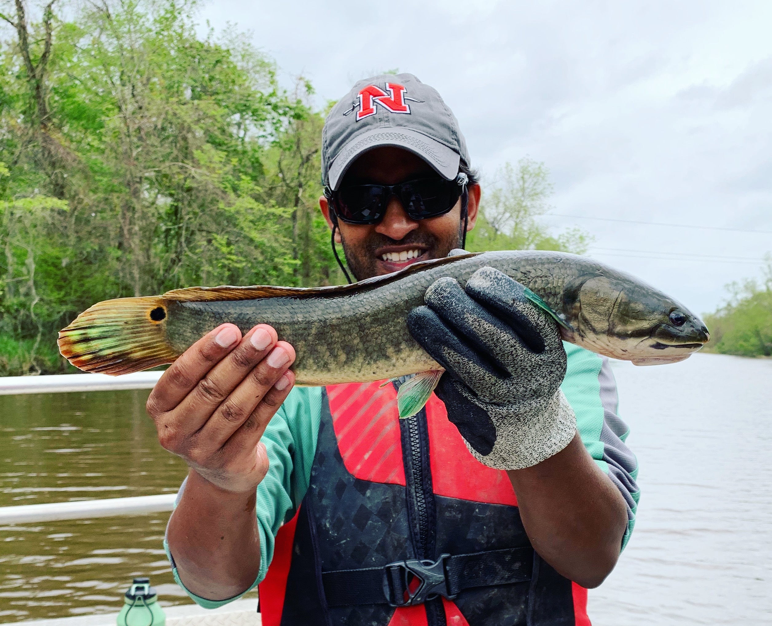 Man with hat smiles holding a medium-sized bowfin fish. It has bright green fins