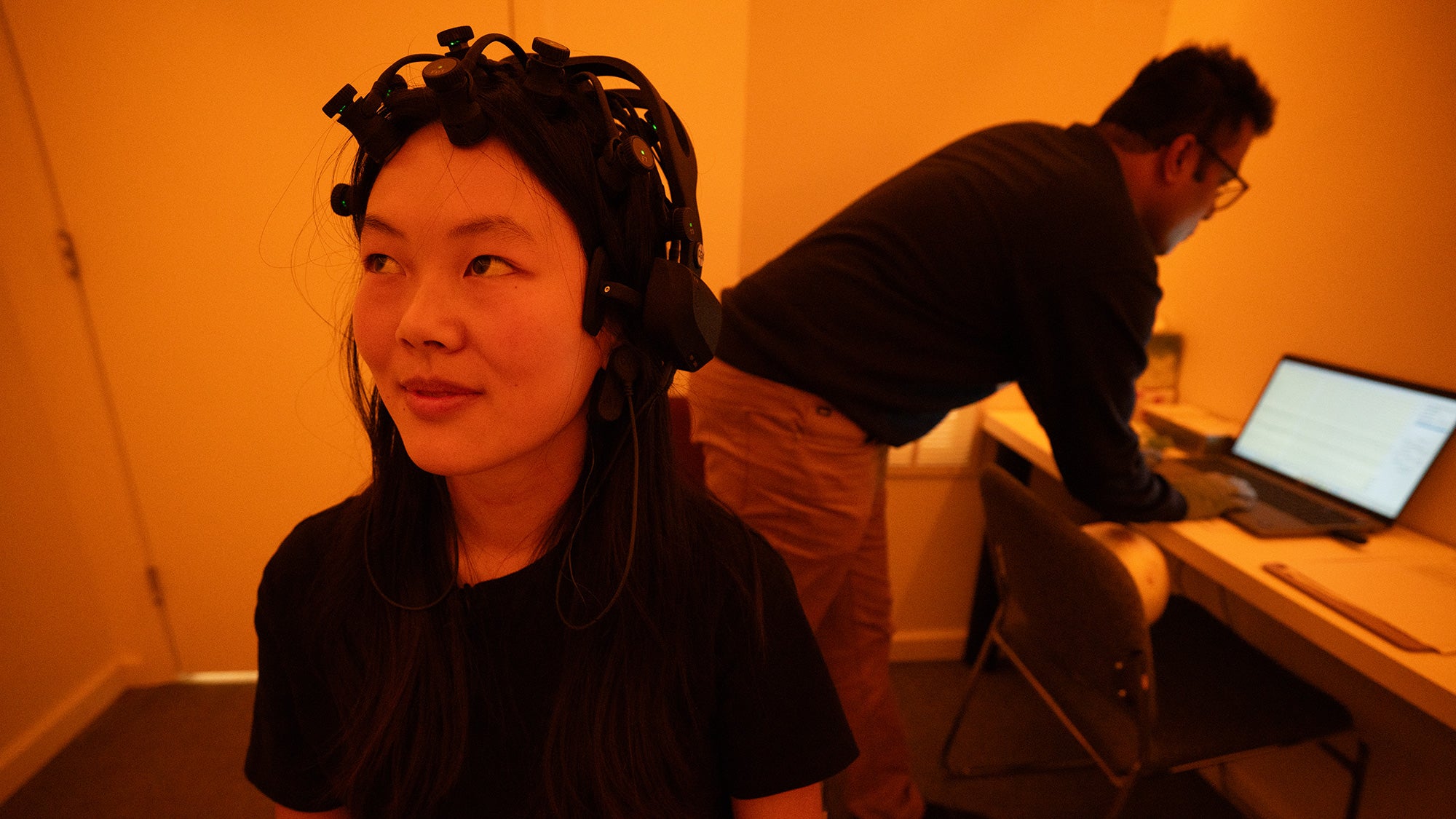 Student sits with EEG equipment on her head in a room lit with amber light