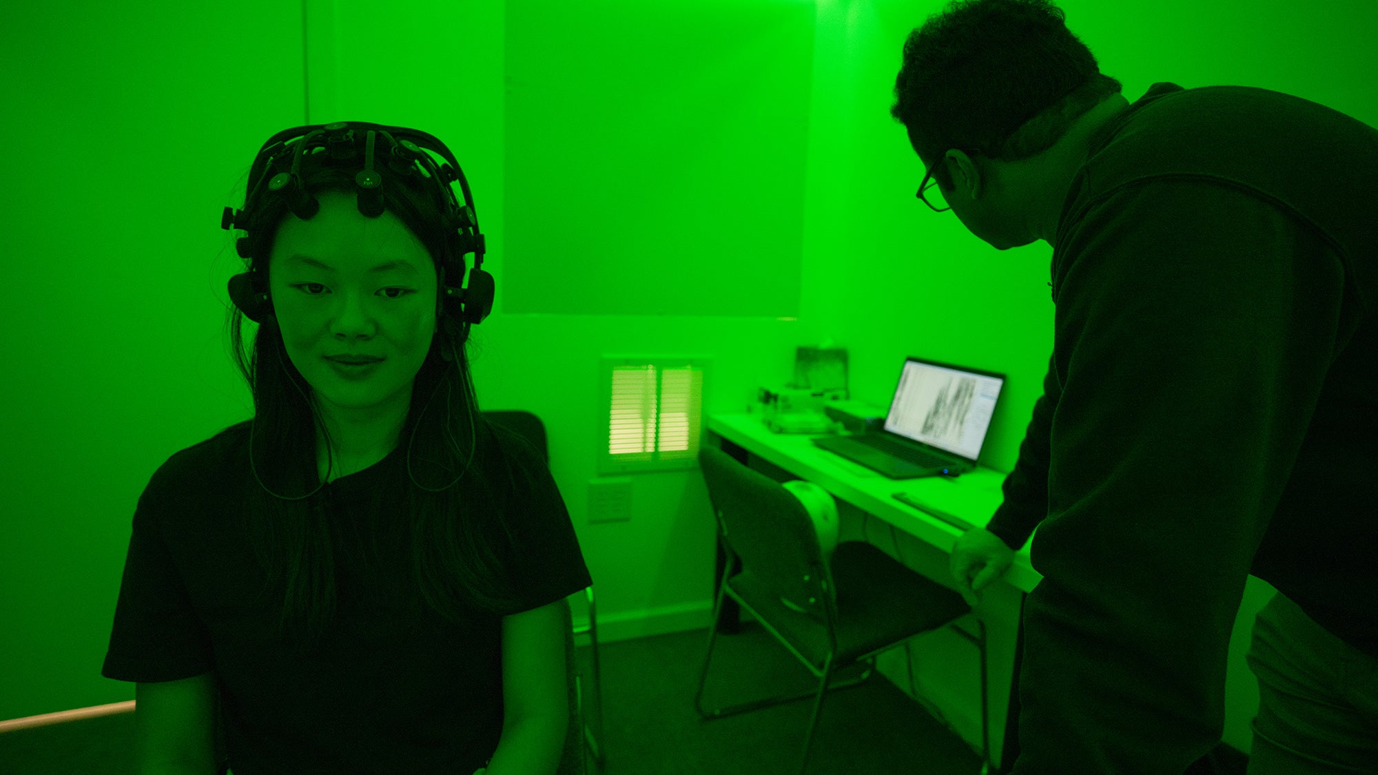 Student sits with EEG equipment on her head in a room lit with green light
