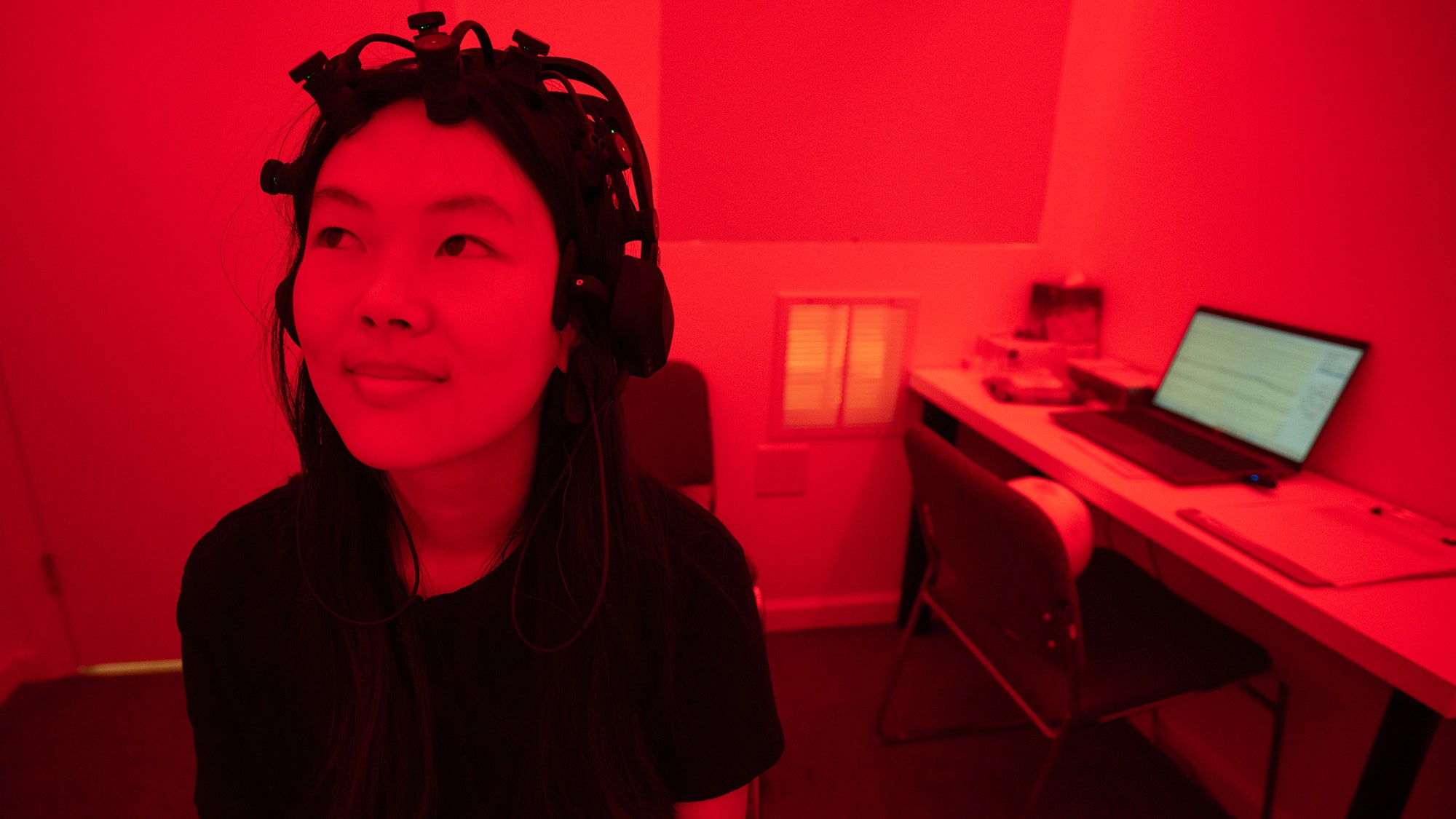 Student sits with EEG equipment on her head in a room lit with red light