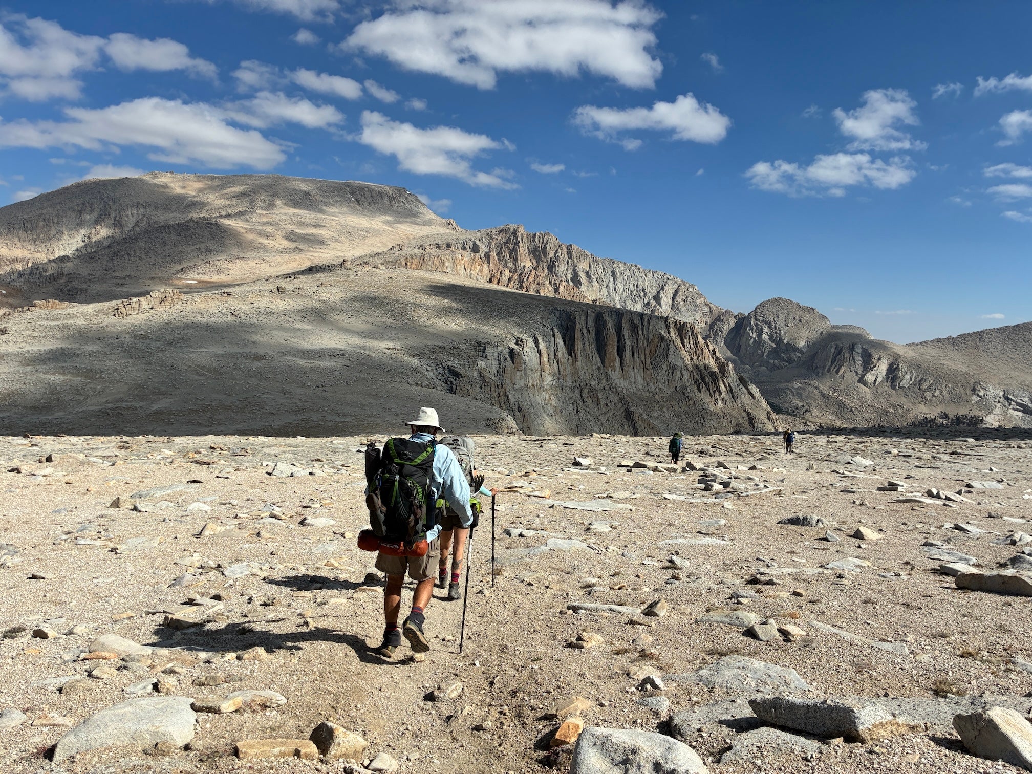 Hikers walk with pole and packs across arid rocky landscape in Sierra Nevada mountains