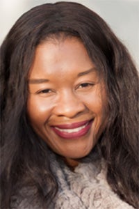 Smiling woman with long, wavy black hair, wearing a light sweater against a blurred background.