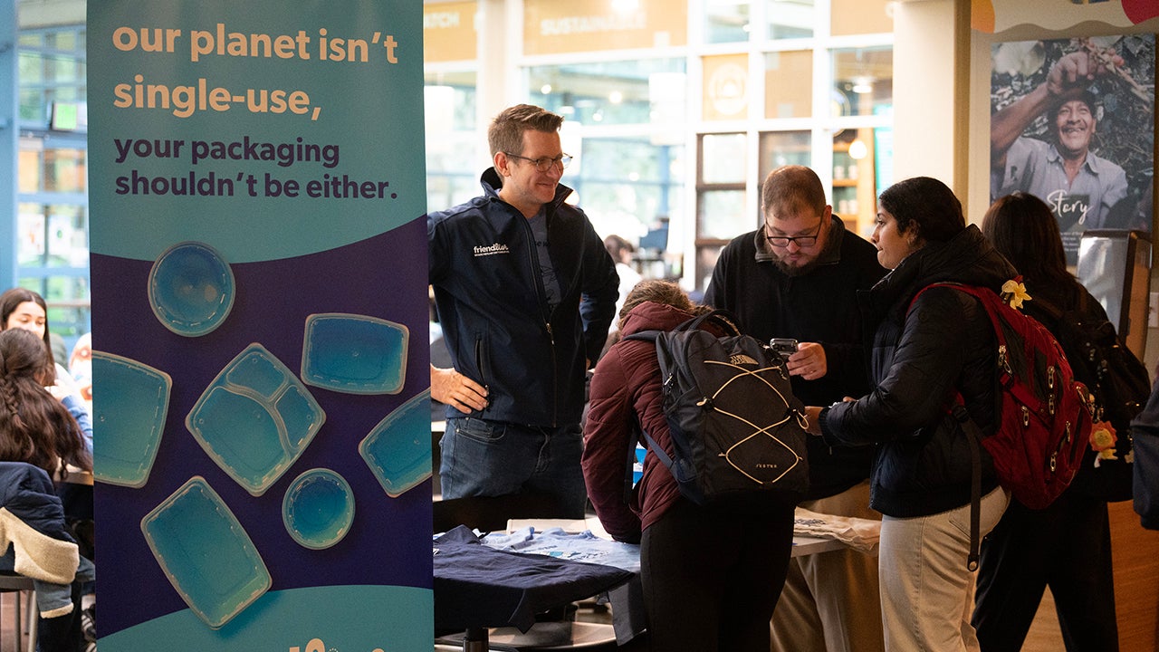 Around a table, students sign up for the app used to scan used containers. 