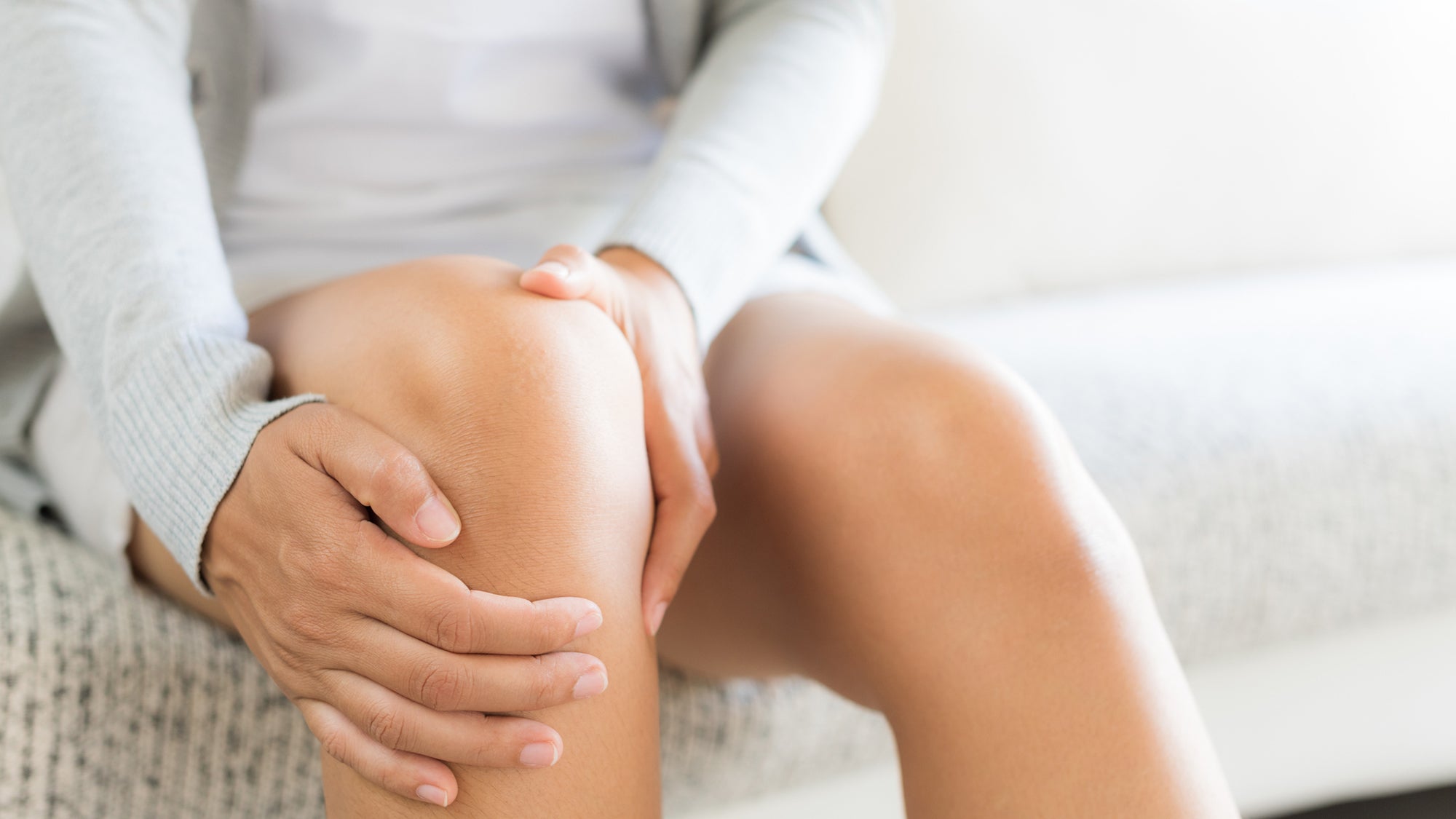 woman sitting on sofa and feeling knee pain