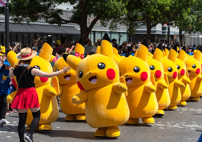A parade of several large, cheerful Pikachu mascots with a crowd in the background.