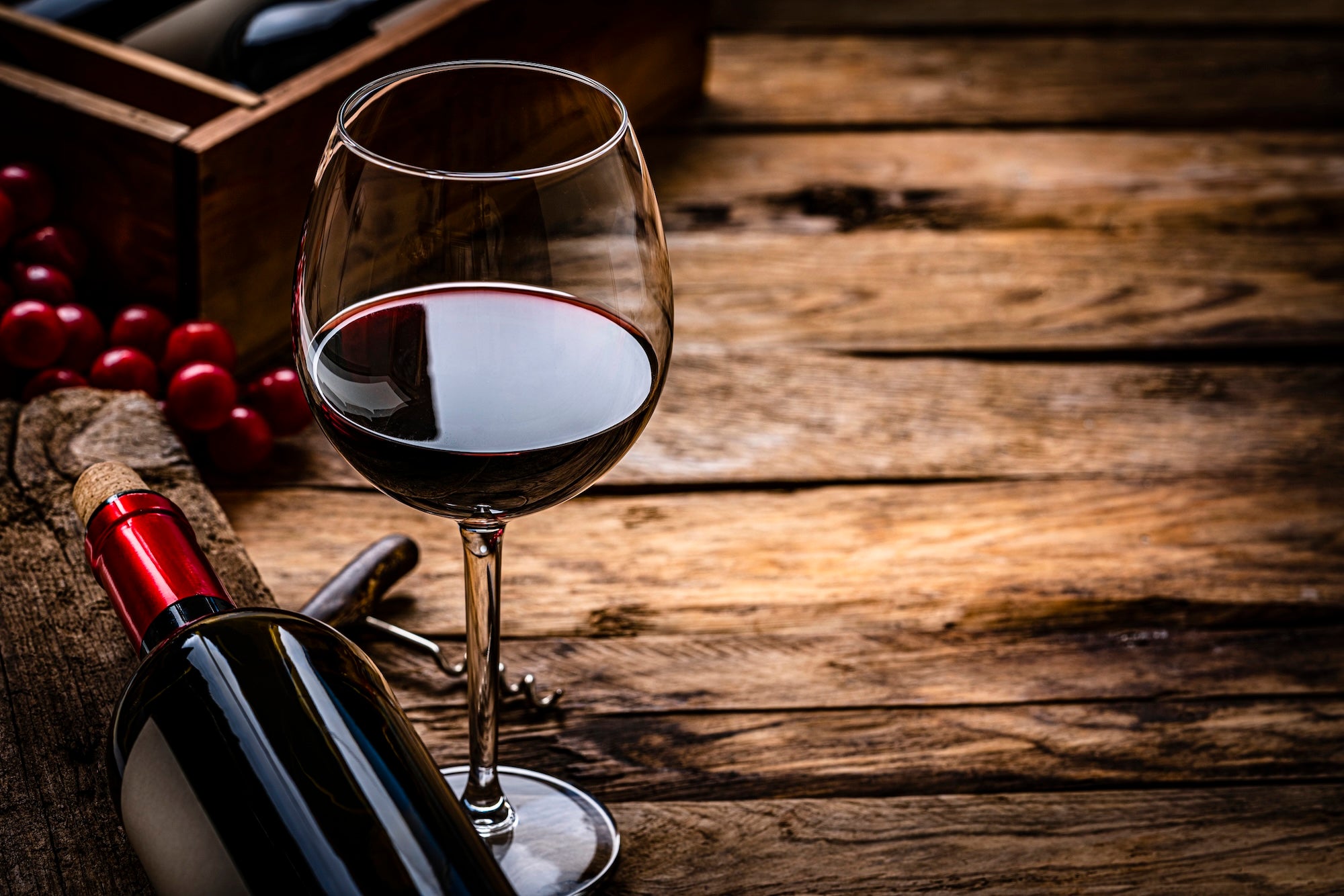 Close up view of a red wineglass shot on rustic wooden table. A wine bottle is laying beside the wineglass. Selective focus on the wineglass. A corkscrew, grapes and a wine bottle box complete the composition. (Getty)