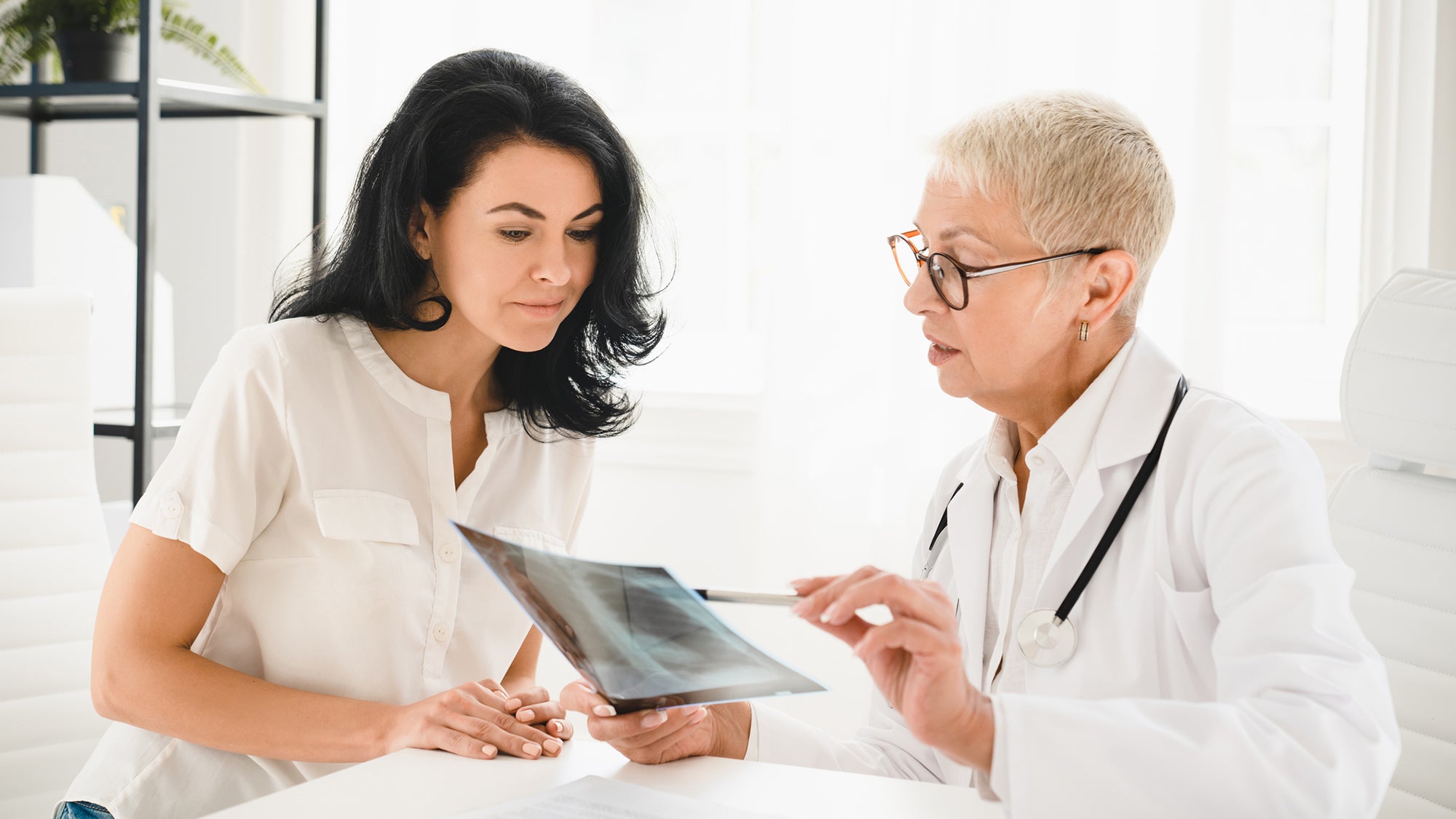 Senior doctor general practitioner showing x-ray lungs photo to female patient
