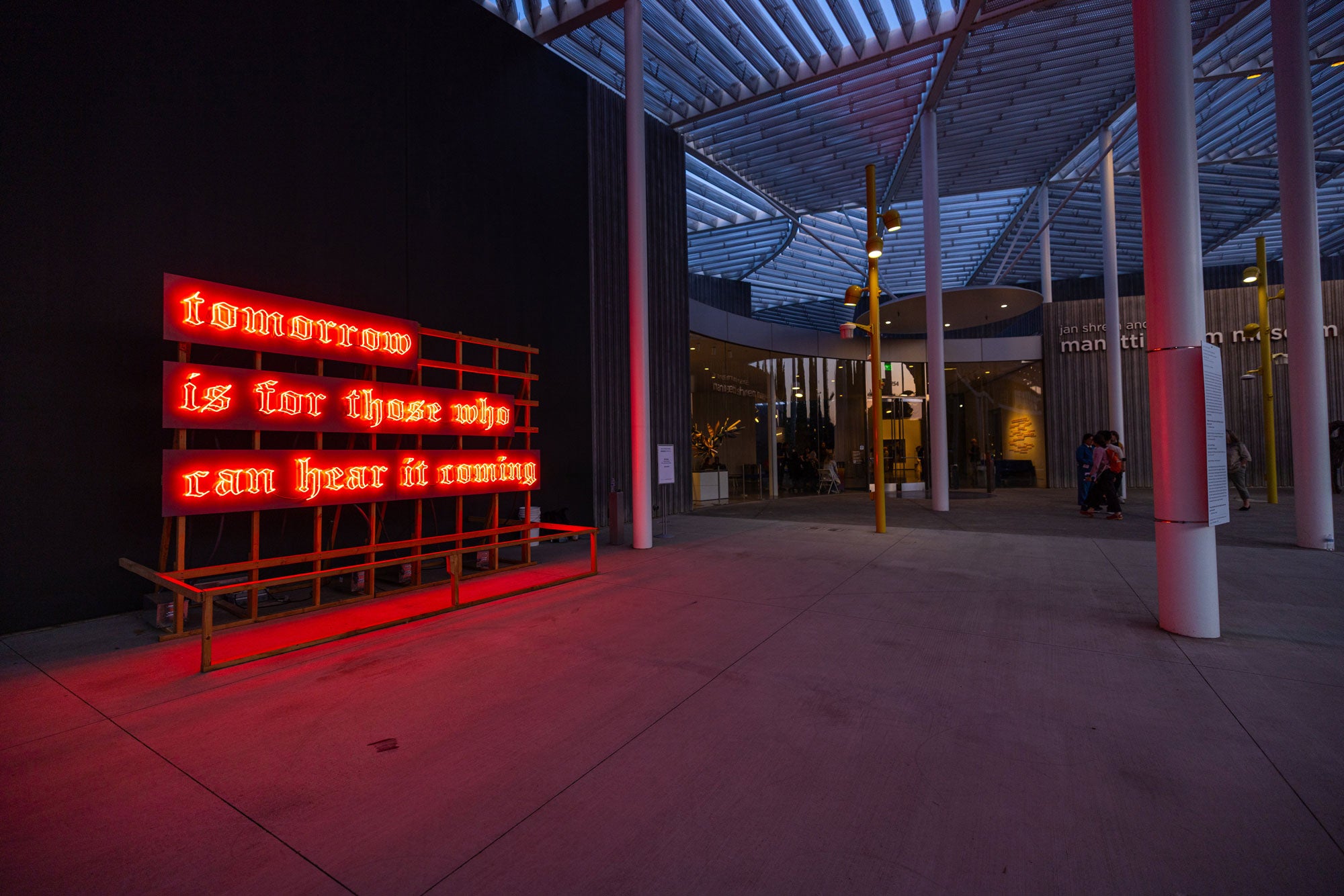 Neon sign, in orange, photographed at dusk in front of museum