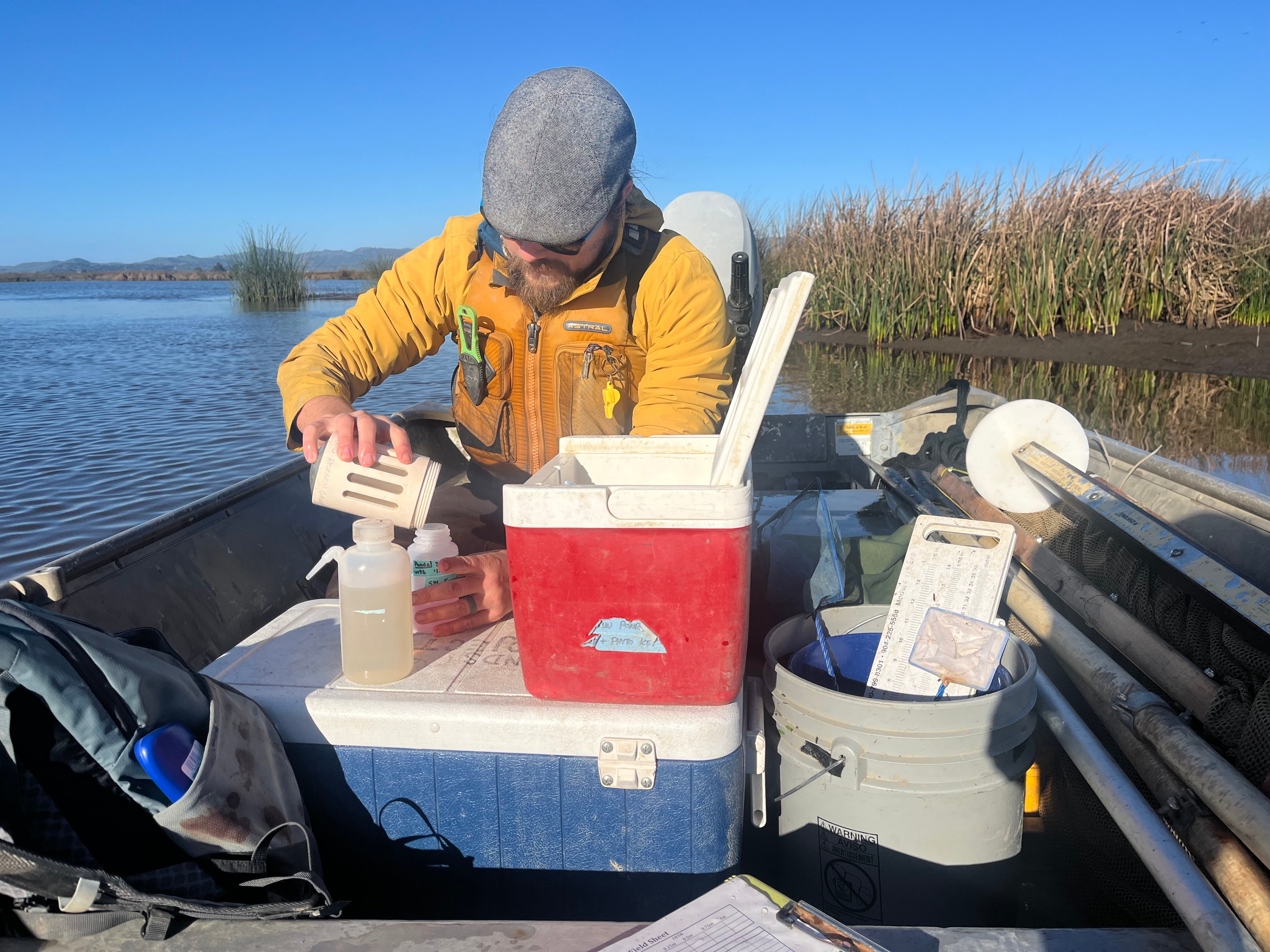 A person in a yellow jacket conducts an experiment on a boat with a cooler and containers.