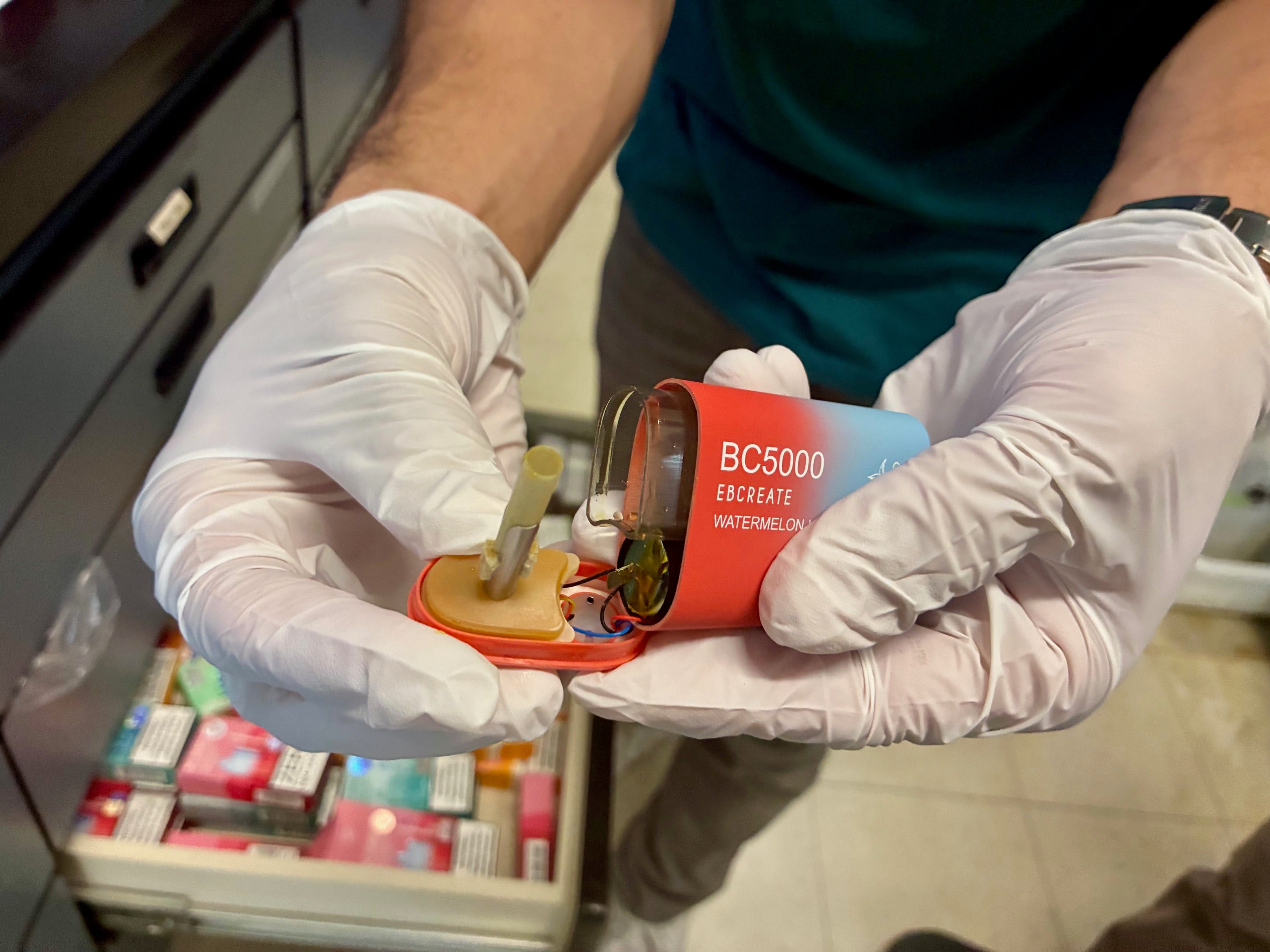 white gloved hands opens disposable, red and blue vaping pod showing internal components, including battery, coil and e-liquid