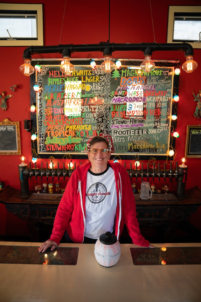 Iva Walton in red jacket in front of a red wall and behind the bar at Mei Wah