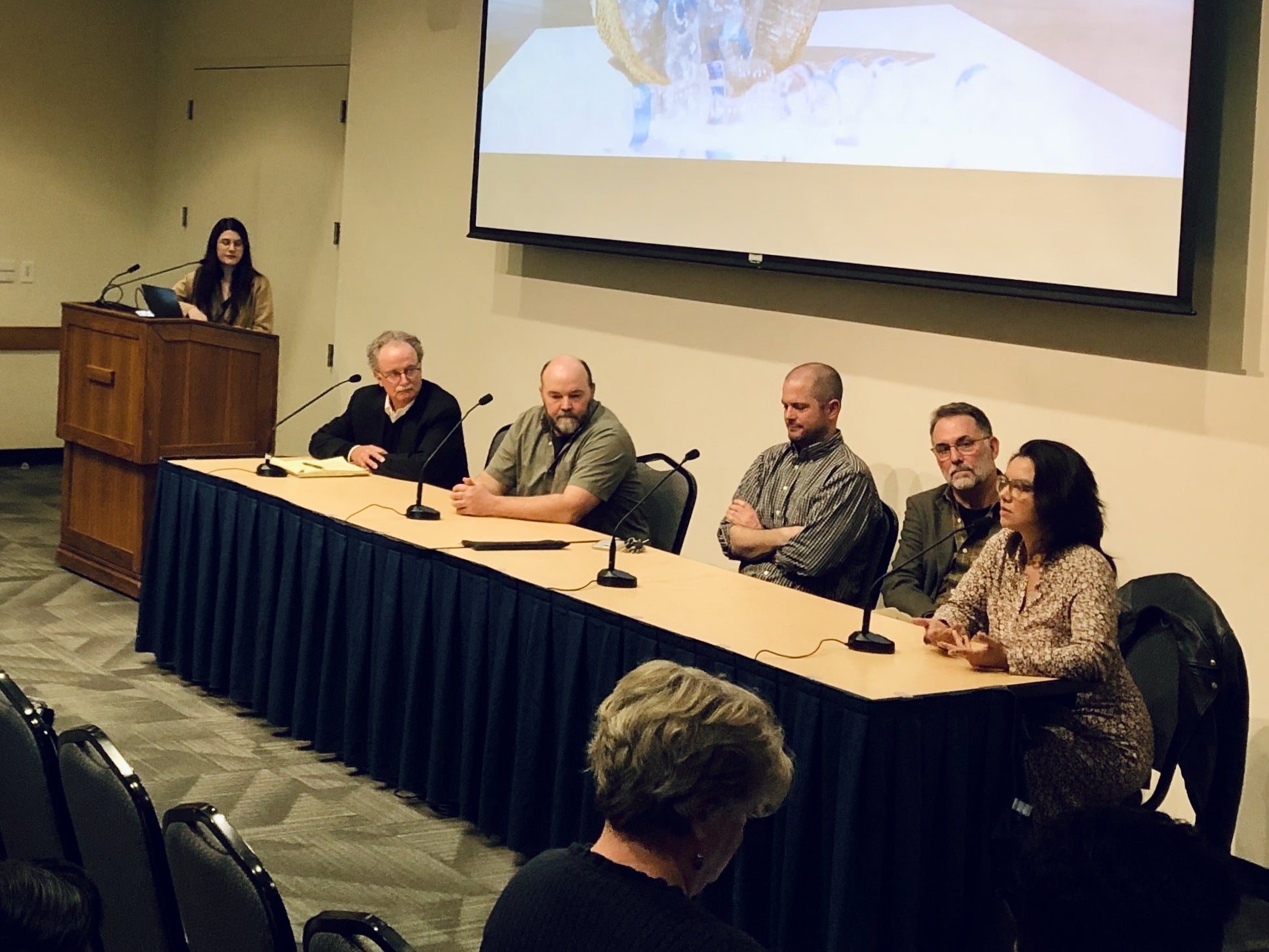 five panelists and a moderator sit at a table facing the audience