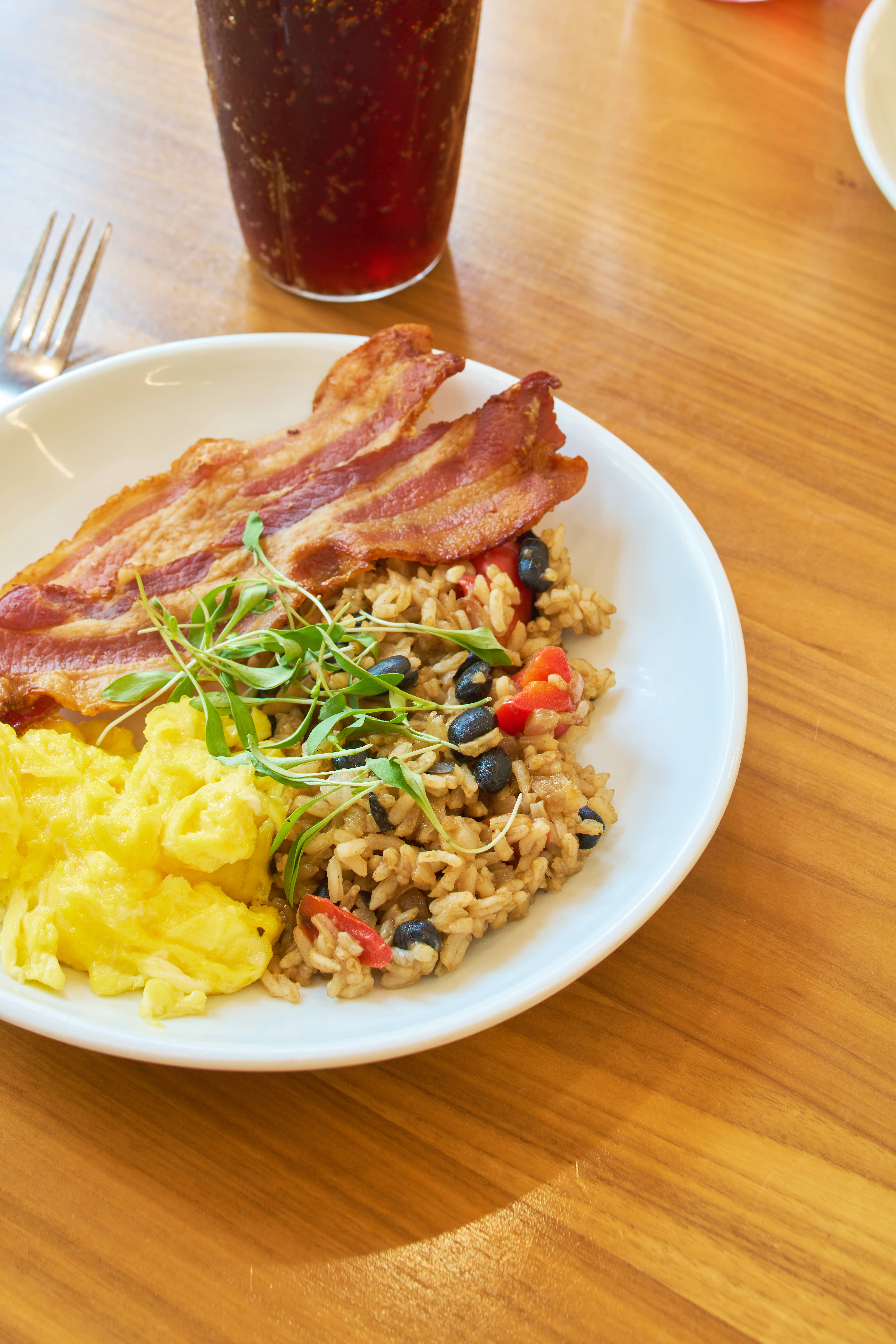 A plate of breakfast food, featuring scrambled eggs, bacon and quinoa, rests atop a wooden table inside a dining common at UC Davis. 