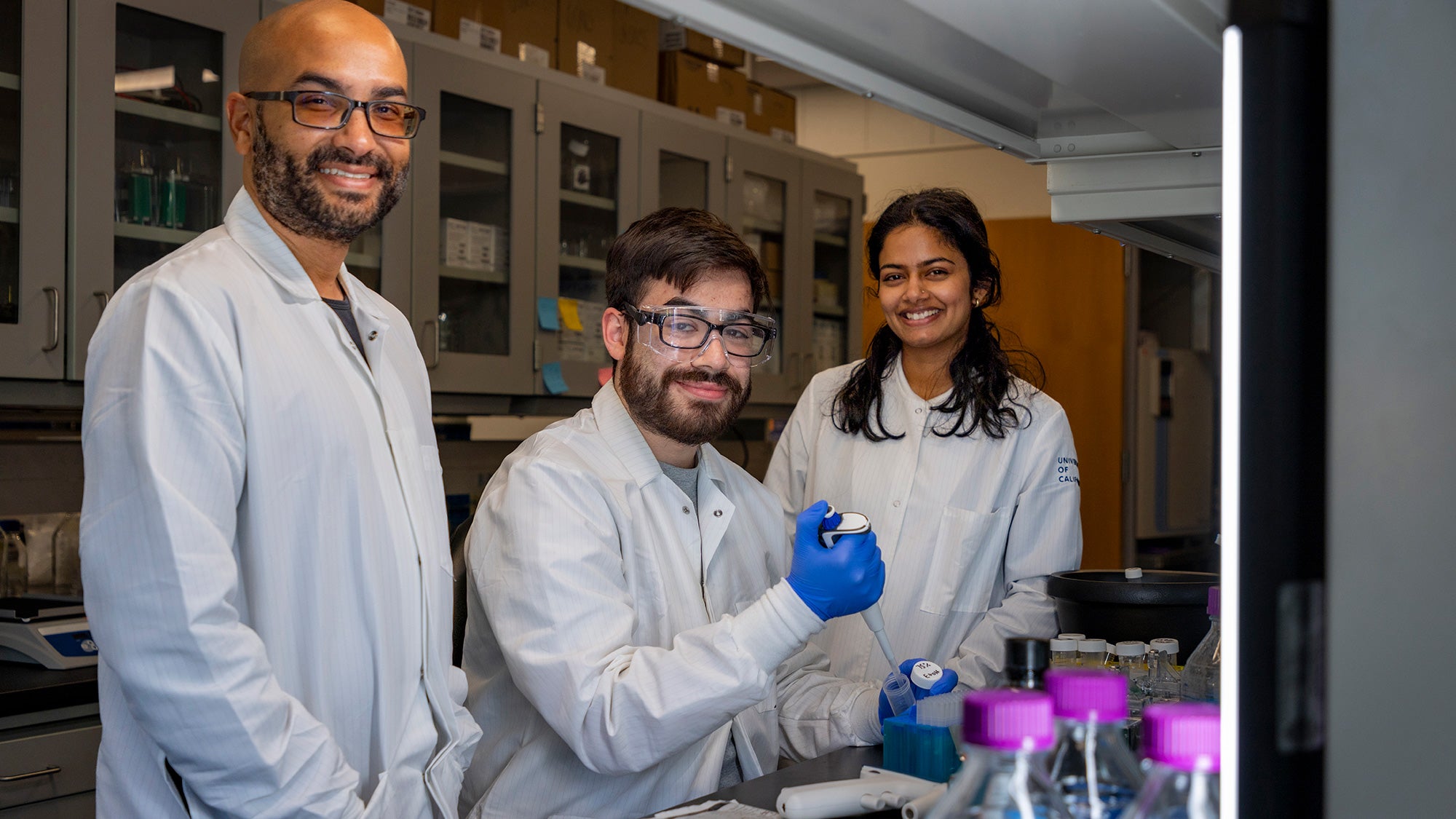 Three researchers in lab coats smile for the camera
