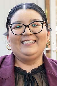 Smiling woman with glasses, maroon blazer and gold hoop earrings