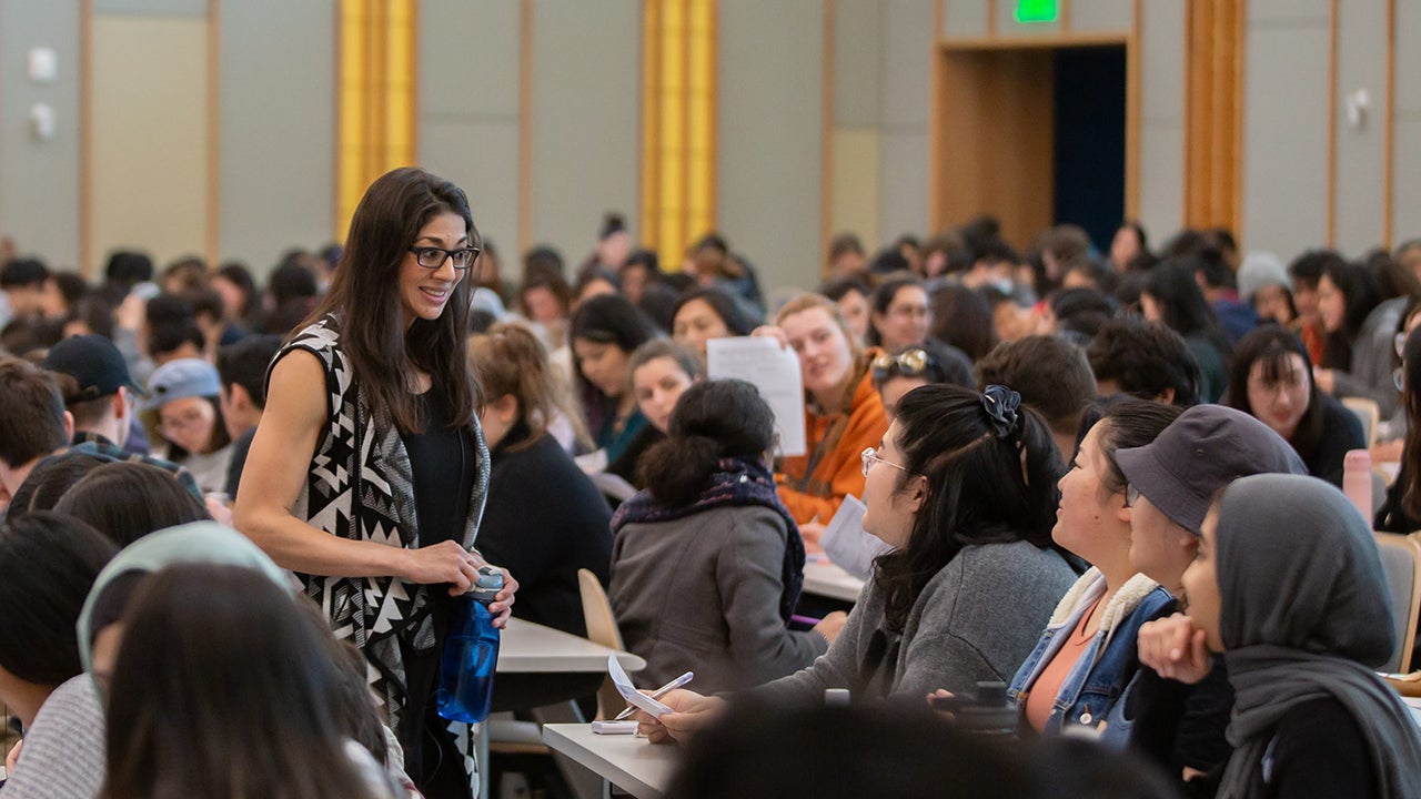 Marina Ellefson stands and talks with seated students in a large classroom