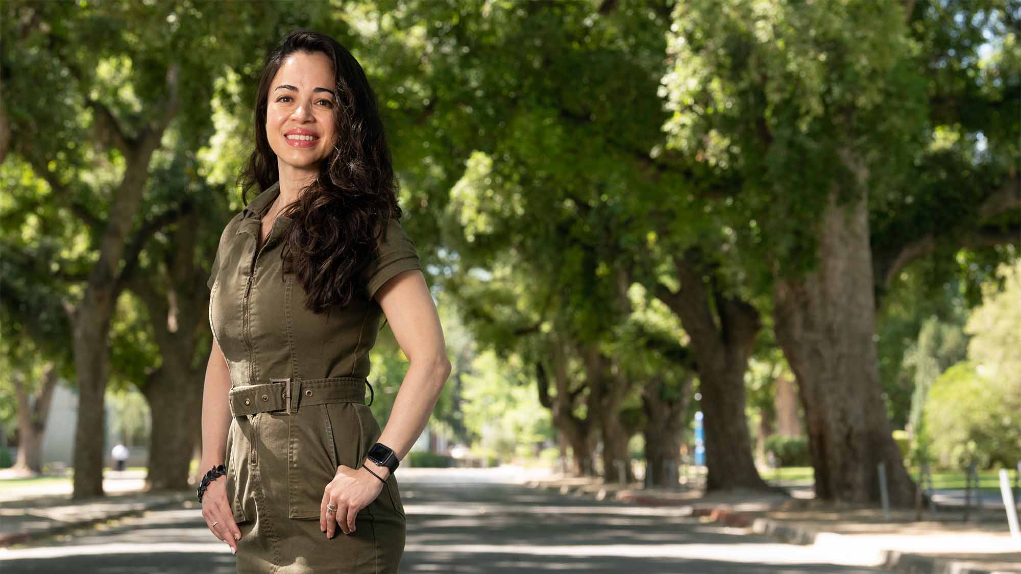 Person wearing green jumpsuit poses for photo on tree-lined West Quad Avenue.