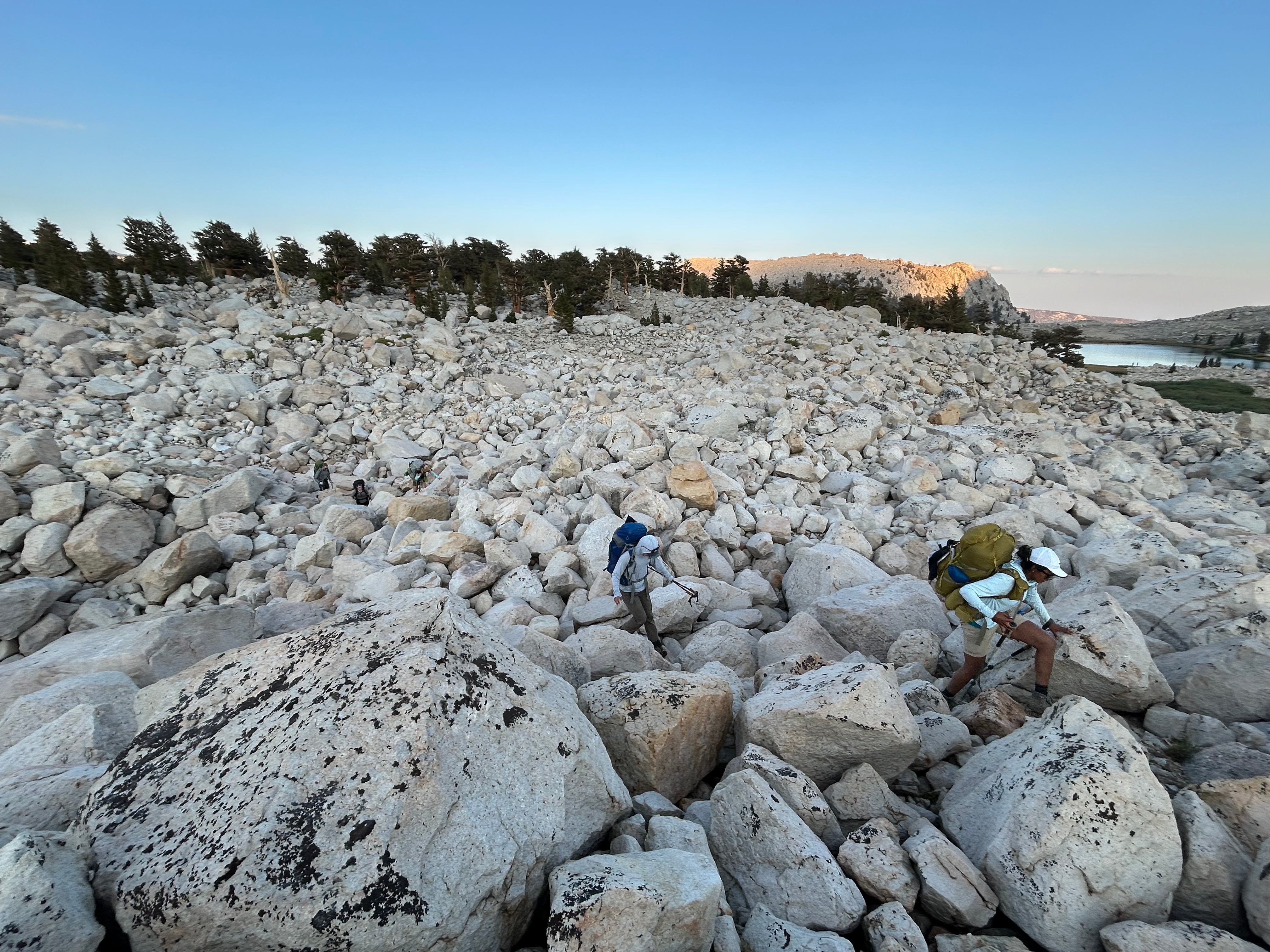 A man and woman hunch over while traversing a large boulder field in the eastern Sierra Nevada mountains 