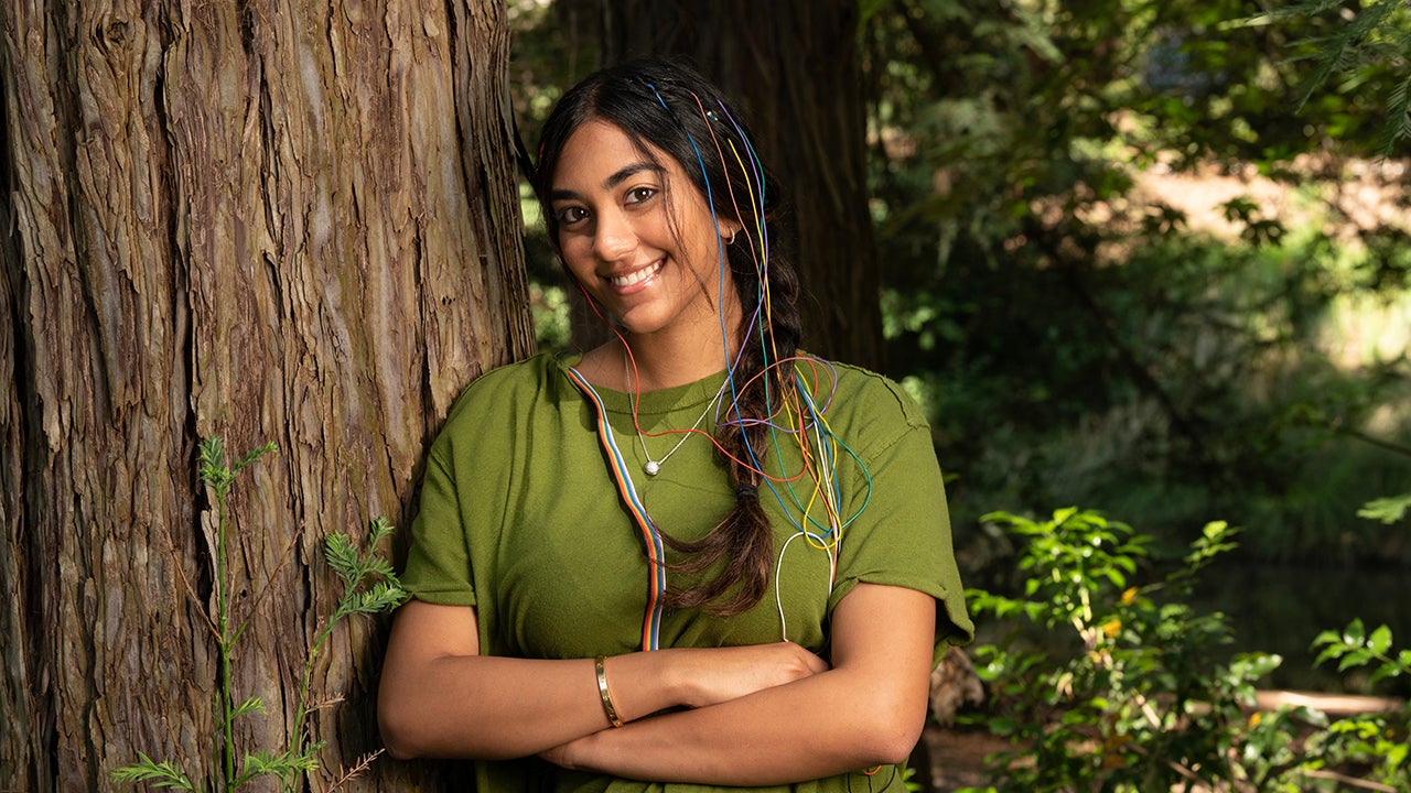 With colored wires from an electroencephalogram showing in her hair, Nikhita Toleti leans against a large tree