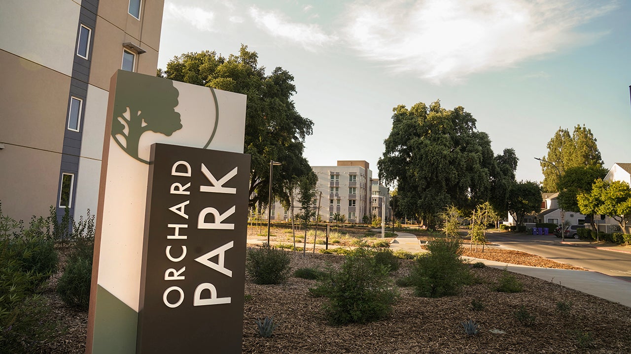 An Orchard Park sign beside an apartment building showing landscape and paths in the background