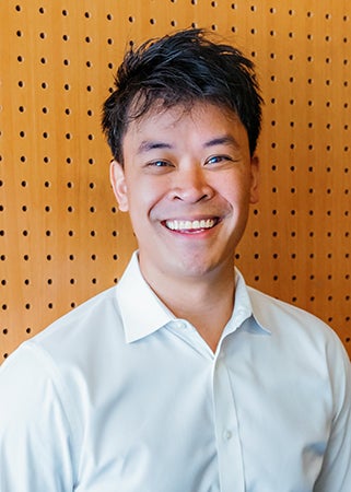 Smiling young man in white shirt headshot against pegboard background