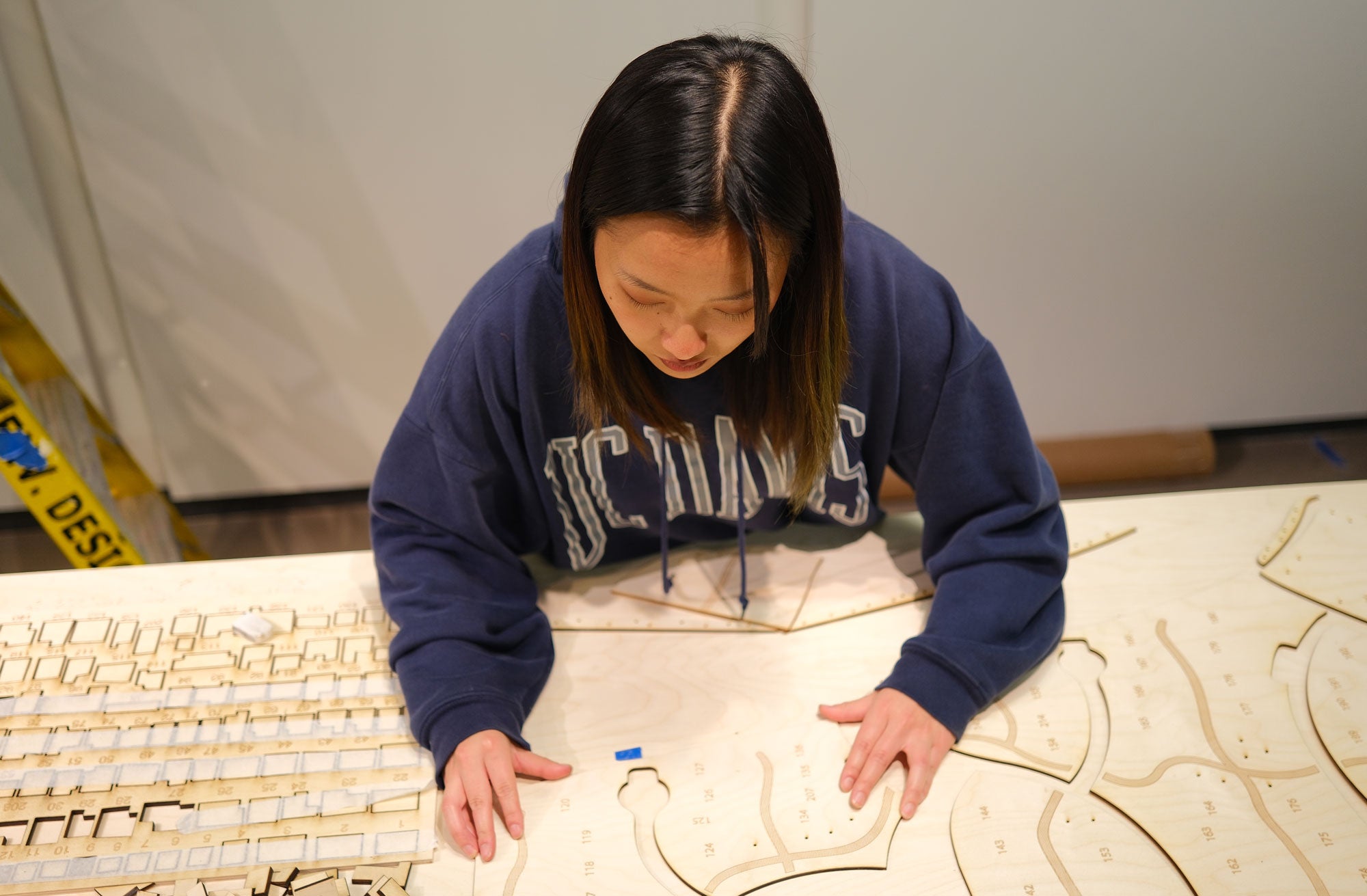 Student with long dark hair and sweatshirt works on plans
