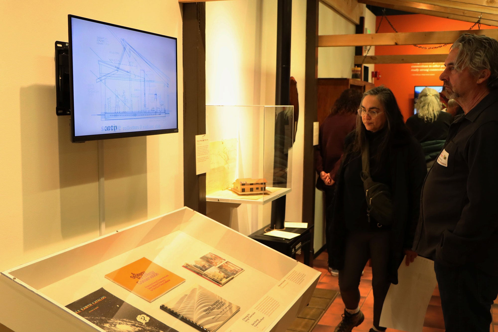 Visitors observing an exhibit with a screen and display case of books.