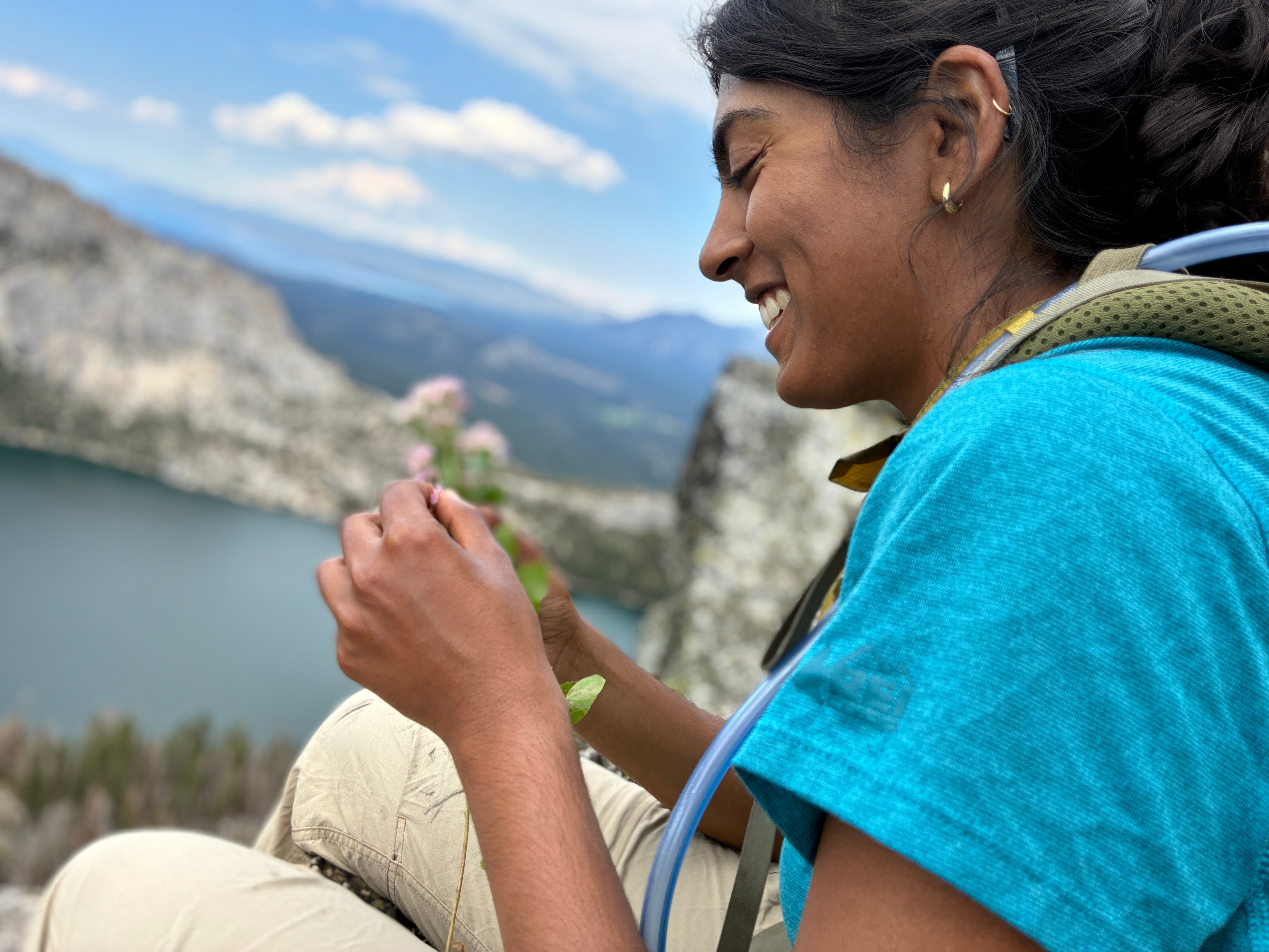 Sachi Srivastava, seen from her profile, smiles in blue tee shirt while overlooking mountains and lake. 