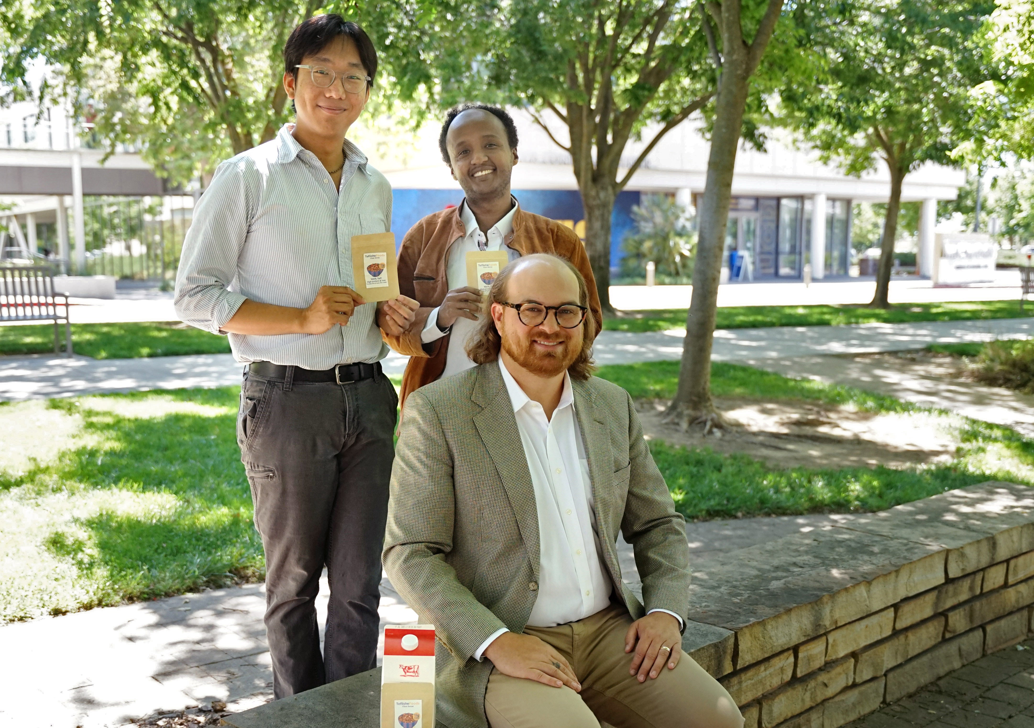 Three people pose with containers labeled "TeflicheFoods: 100% Teff High protein & iron"