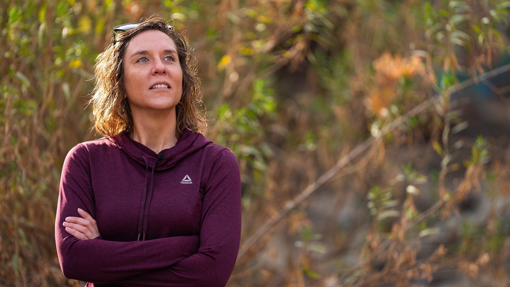Woman stands outside with her arms crossed and looks up