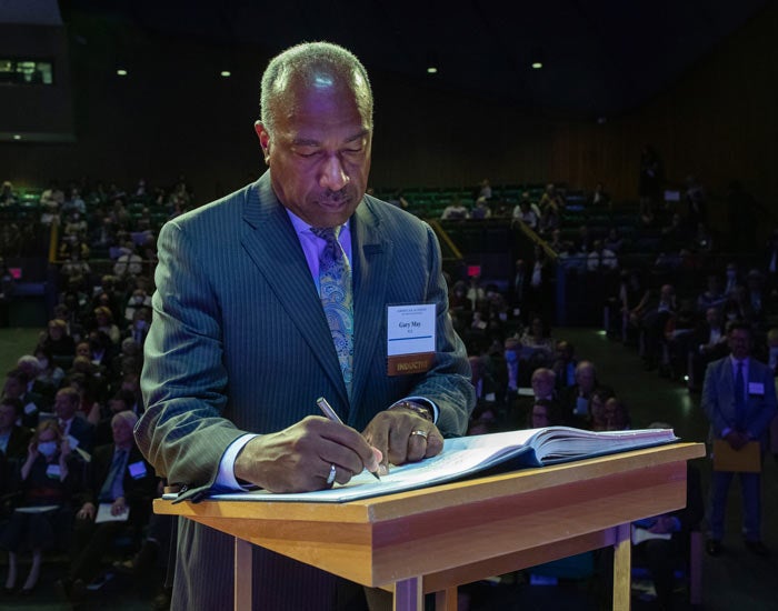 Gary S. May, UC Davis chancellor and faculty, in suit, signs book, at podium, in front of audience