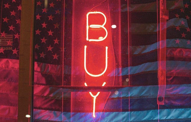 Red neon sign that spells BUY between American flags