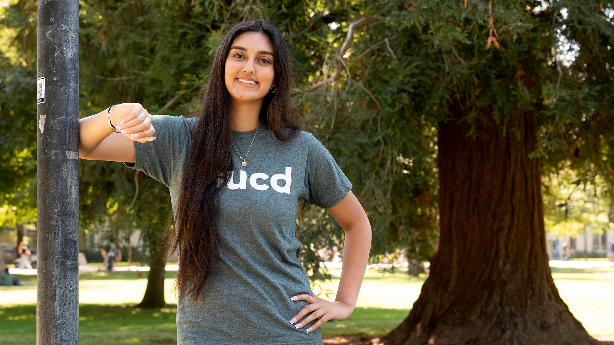 Woman leans against a light pole on the UC Davis Quad