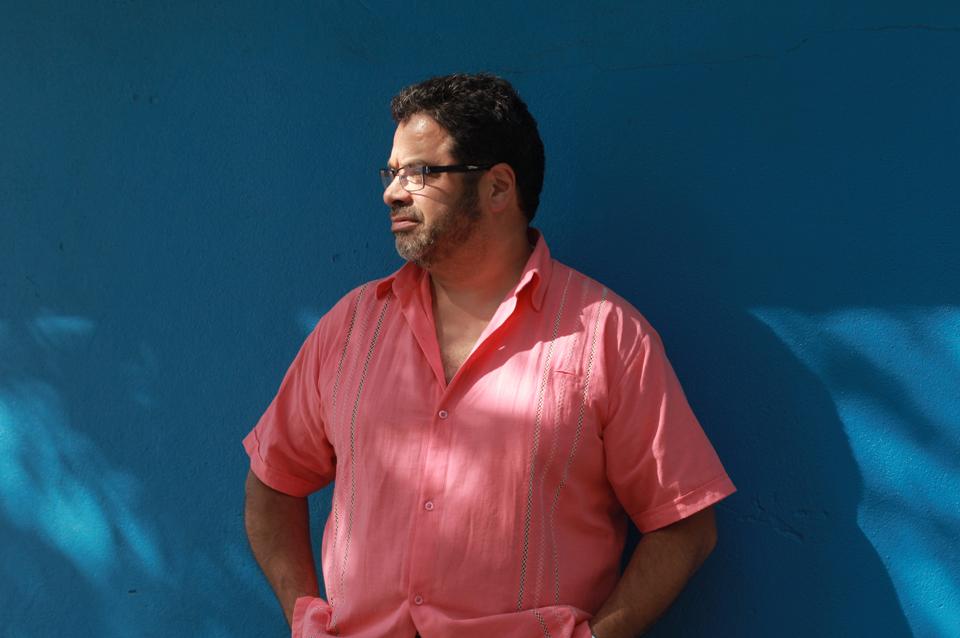 Man in orange shirt with blue background.