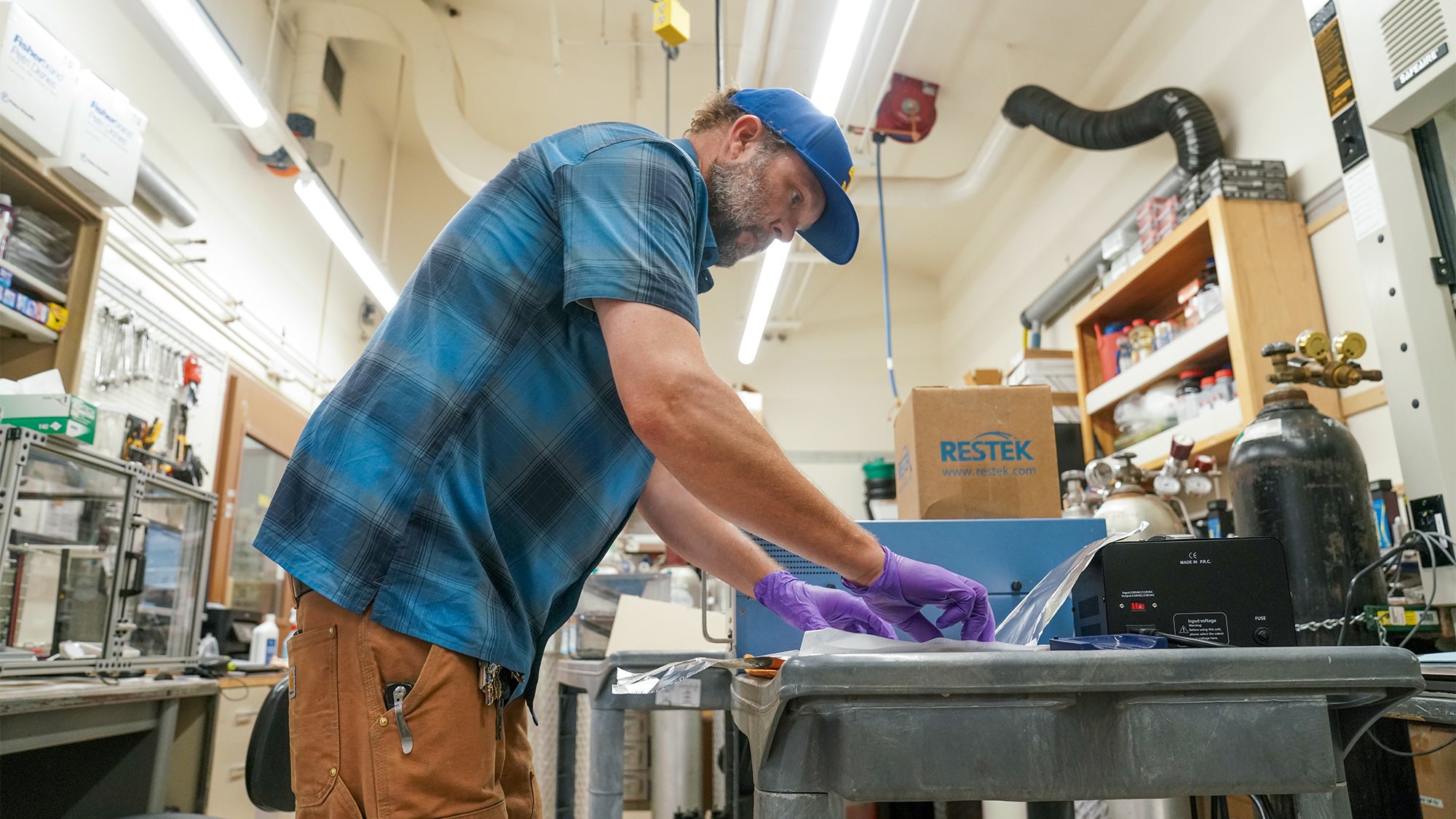 Dr. Keith Bein leans over a table in a large lab area, working on a project that involves foil and small panels.