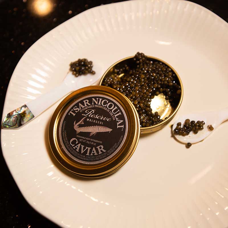 Closeup photo of a white plate with an open tin of caviar. Caviar is also on the plate.