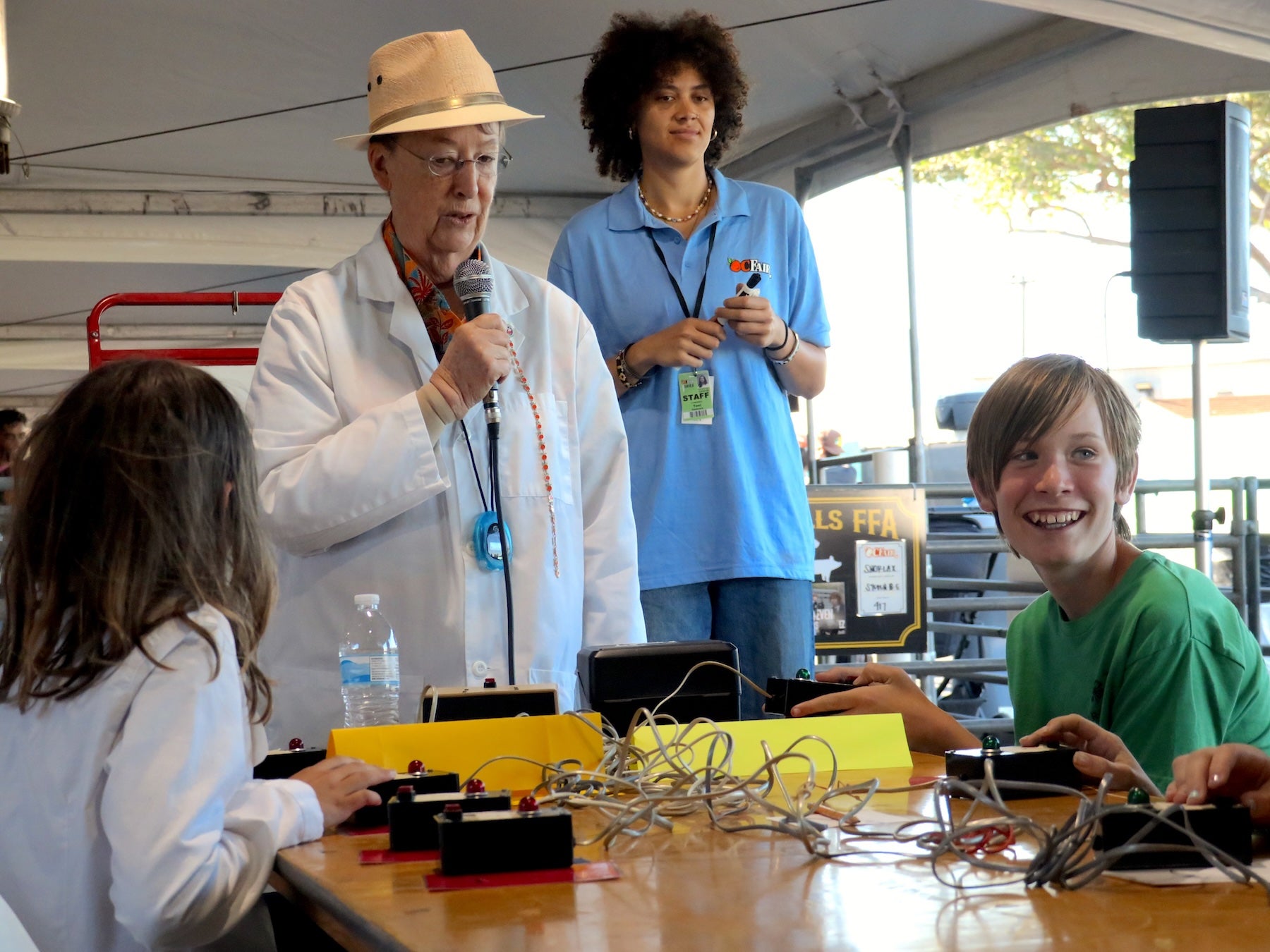 4-H members participate in the avian bowl at the Orange County Fair. They sit at a table with buzzers in front of them. A woman at the head of the table holds a microphone while quizzing two young participants. (Caroline Champlin/UCANR)