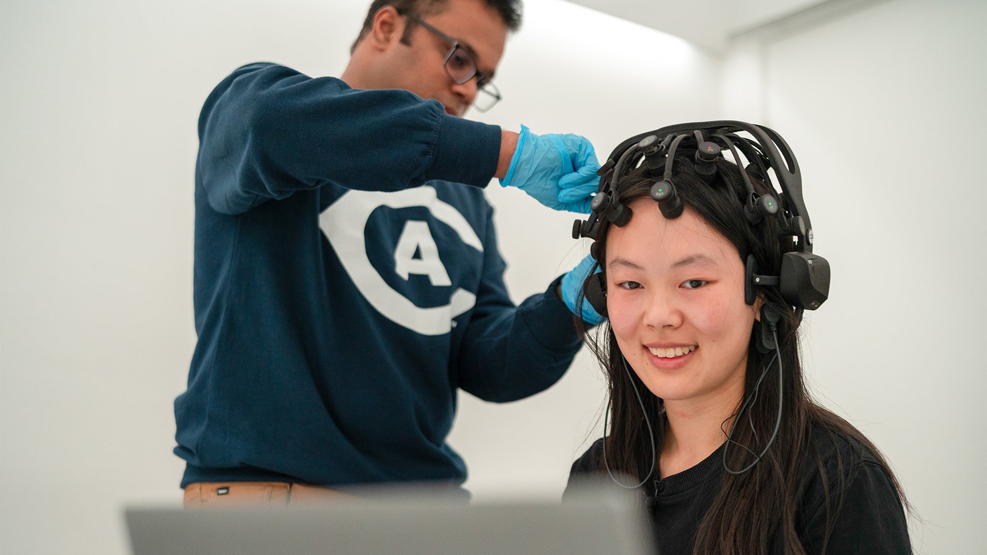 A researcher fits a headset with EEG sensors onto a student to measure brain wave activity during an experiment at UC Davis.