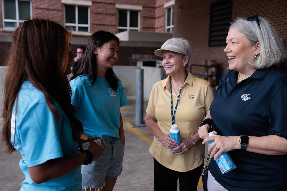 Two female students talk with two university administrators on a college campus.