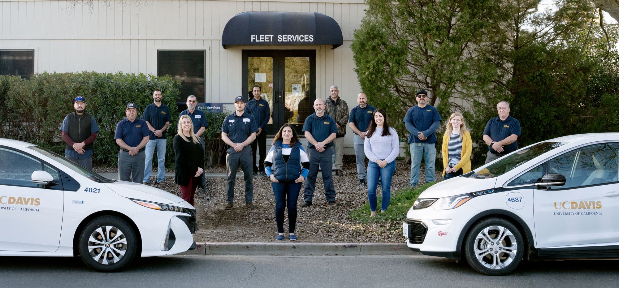 Fleet Services crew, 6-feet distanced, posing, behind two UC Davis cars
