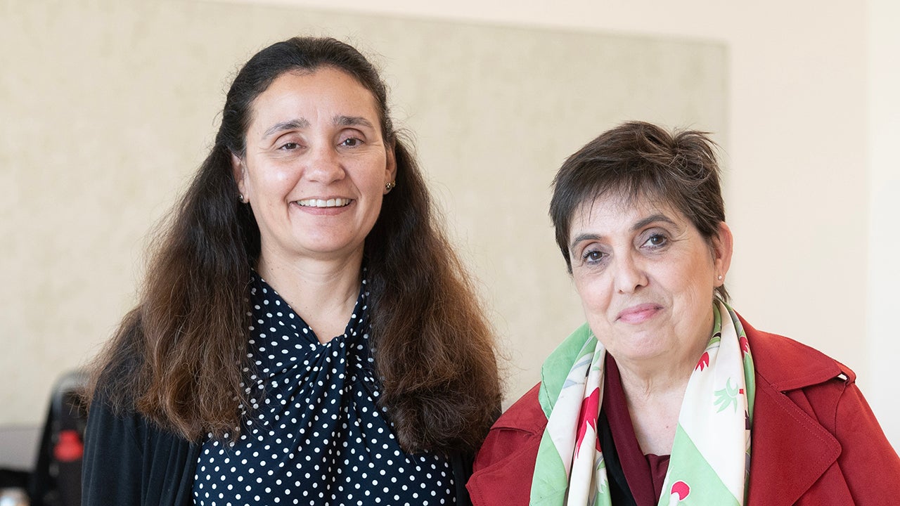 Two women smiling together indoors, one wearing a polka dot top, the other in a red jacket.