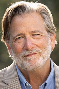 Smiling man with gray hair and a beard, wearing a blazer over a blue shirt.